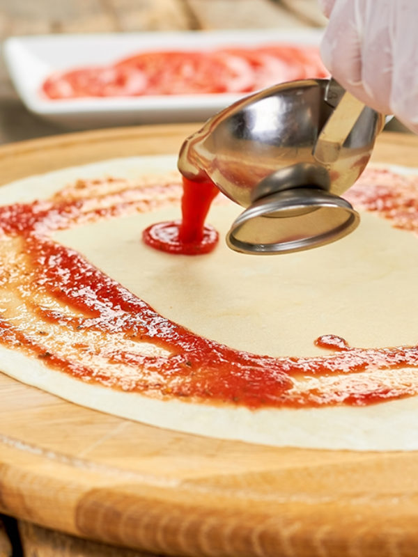 Sauce boat pouring tomato sauce. Hand pouring red sauce on pizza crust from sauce boat.